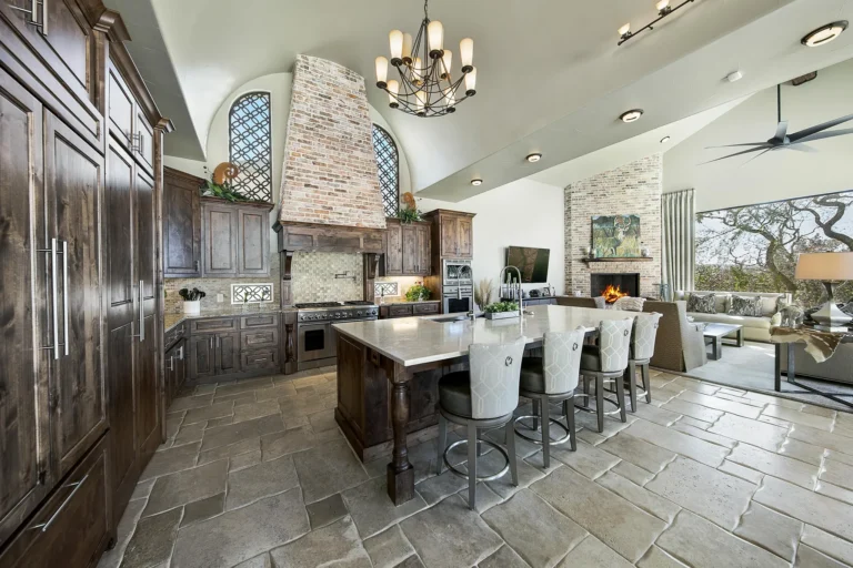 Old-world custom kitchen with knotty alder cabinetry, a brick range hood, wrought-iron chandelier and island seating open to a fireplace family room