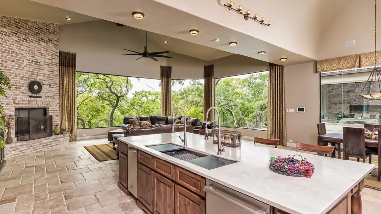 Kitchen island with a white quartz top and alder base, open to a family room with a brick fireplace and walls of windows to the oaks