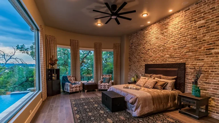 Primary bedroom with a curved brick accent wall, leather headboard and a picture window overlooking the pool and Hill Country