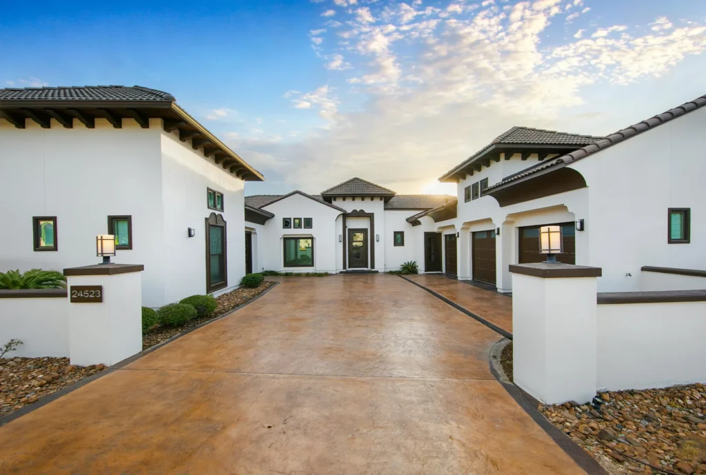 White stucco Spanish-style custom home with a clay tile roof, stained concrete motor court and lantern-lit entry