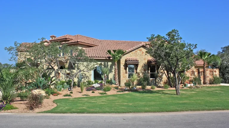 Stone and stucco custom home with a tile roof, palms, agaves and a xeriscaped front yard behind a broad lawn