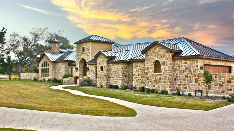 Stone custom home with a standing-seam metal roof, arched entry tower, cupola and curving front walk at sunset
