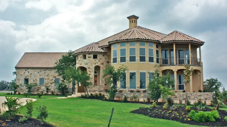 Two-story stone and stucco custom home with a round stone turret, curved wall of windows, second-floor balcony and cupola