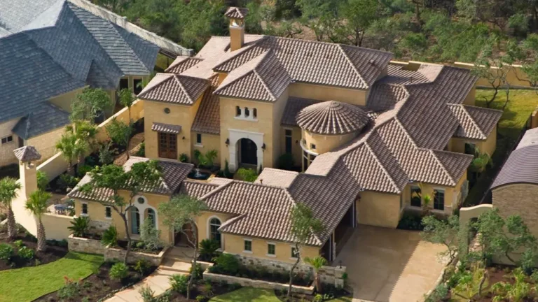 Aerial view of a Tuscan-style stucco custom home with a tile roof, round tower, arched entry and landscaped courtyards