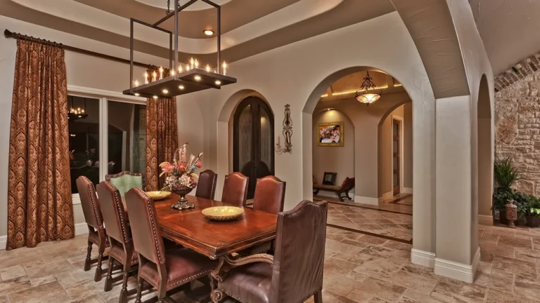 Formal dining room with an iron candle chandelier, leather chairs, arched openings and a stacked-stone wall