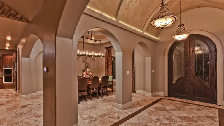 Foyer with arched mahogany and wrought-iron double doors, a vaulted ceiling, iron pendants and travertine floors