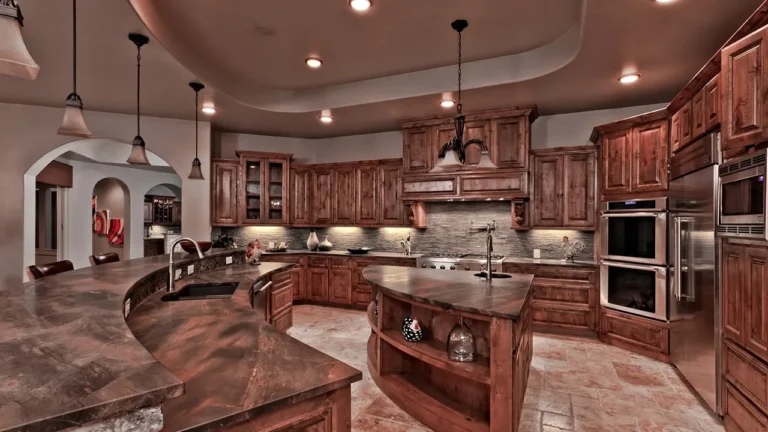 Dark alder kitchen with a curved granite bar, island prep sink, double wall ovens and pendant lights under a tray ceiling