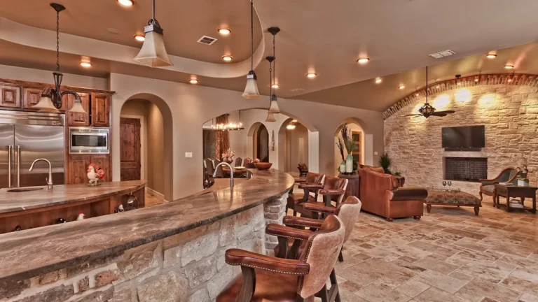 Kitchen with a stone-faced raised bar and leather stools open to a family room with a stone fireplace