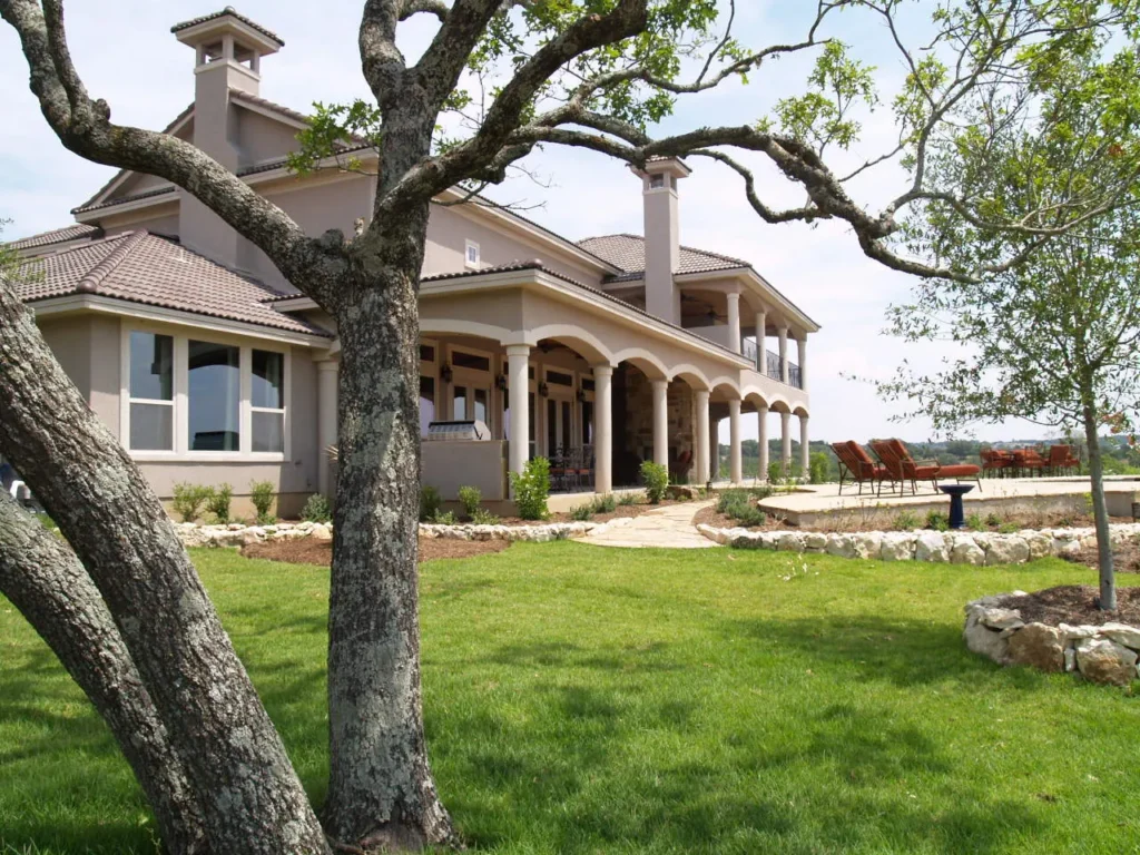 Arched rear loggia and covered porch framed by a live oak at a Mystic Shores home overlooking Canyon Lake