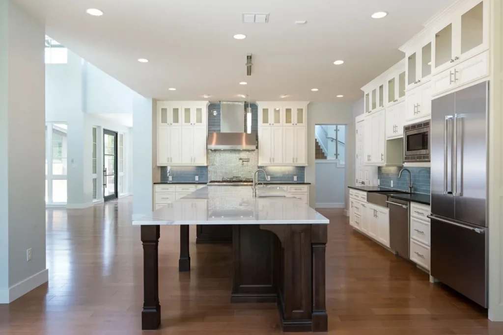 White kitchen with glass-front upper cabinets, a dark stained island with turned legs and hardwood floors in a North San Antonio custom home