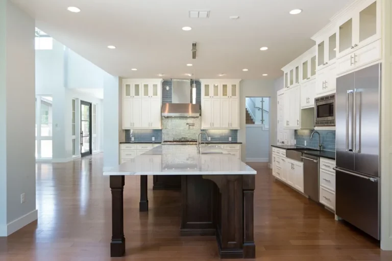 White kitchen with glass-front upper cabinets, a dark stained island with turned legs and hardwood floors in a North San Antonio custom home