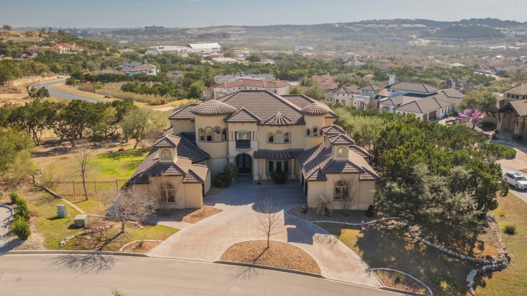 Aerial view of a Mediterranean-style custom estate with tile roofs and a circular motor court on a North San Antonio hillside