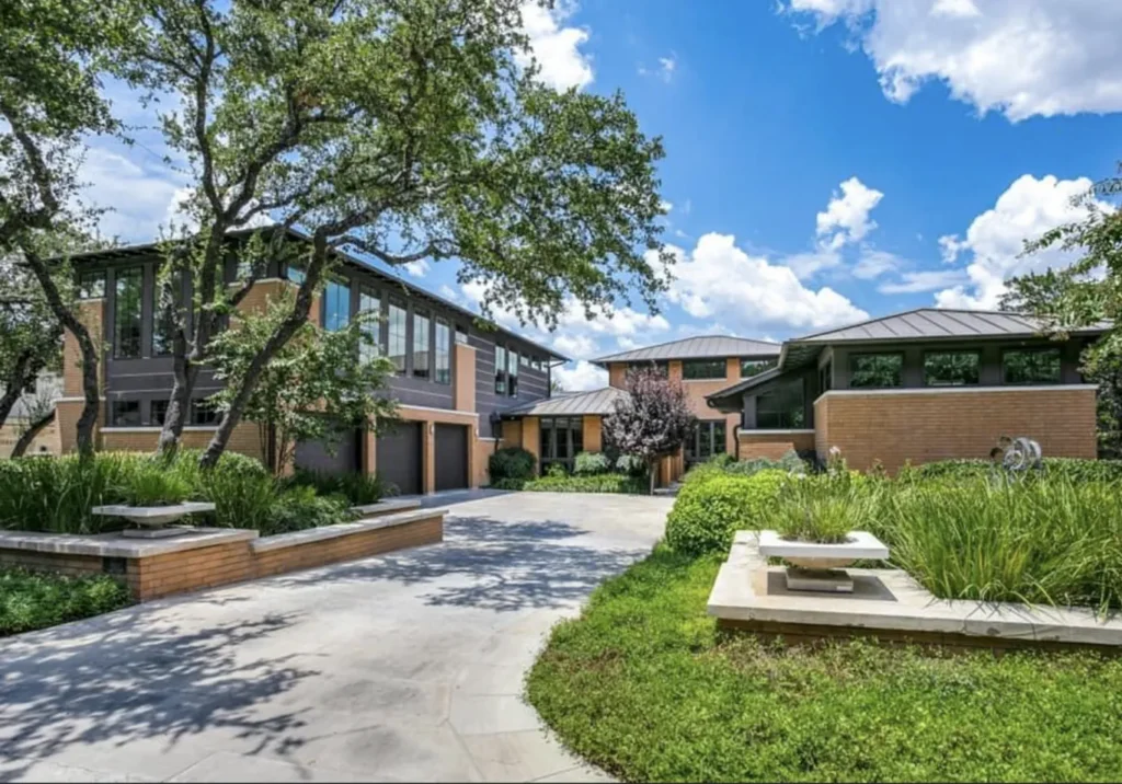 Prairie-modern brick custom home beneath mature live oaks with a landscaped drive and planters in North San Antonio
