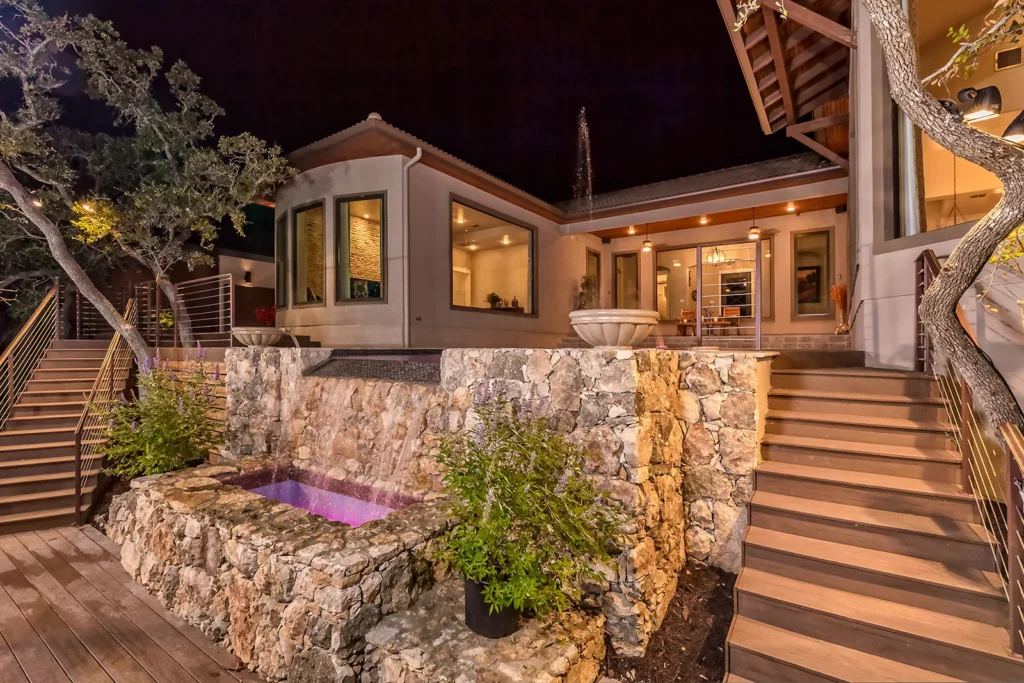 Night view of a stone waterfall spa with color lighting, cedar staircase and covered outdoor living from the Genesis Custom Homes 2015 Parade of Homes entry