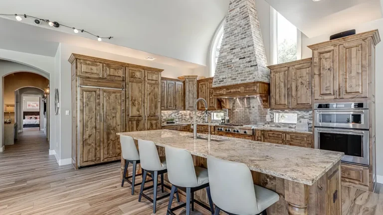 Knotty alder kitchen with a brick range hood, granite island seating, double wall ovens and track lighting in The Dominion, San Antonio