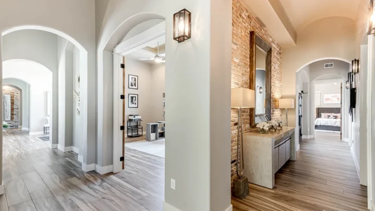 Arched hallway with wood-look tile floors, a whitewashed brick accent wall and iron wall sconce leading to the bedrooms
