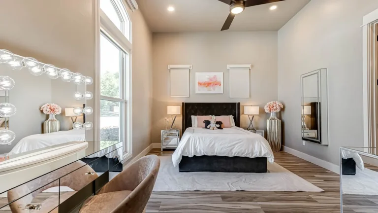 Bedroom with a lighted Hollywood vanity mirror, upholstered bed and tall windows