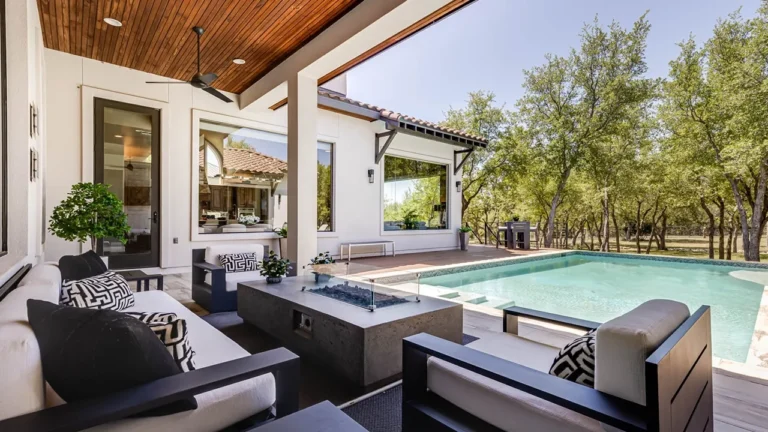 Covered patio with a cedar ceiling, lounge seating and a fire table looking out to the pool and live oaks