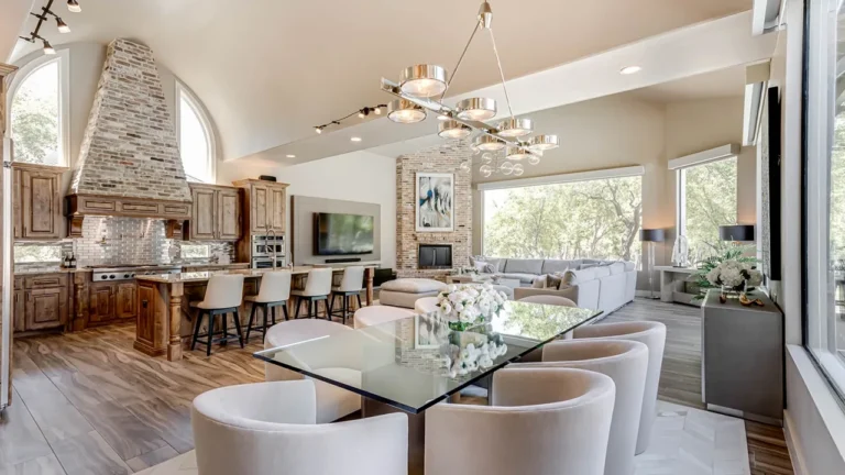 Glass dining table with upholstered swivel chairs beneath a modern ring chandelier, open to the knotty alder kitchen and great room
