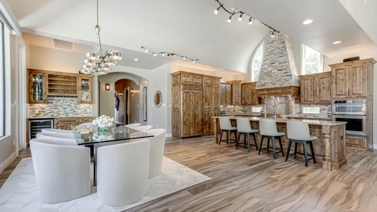 Glass dining table with white swivel chairs and a modern chandelier, open to a knotty alder kitchen with a brick range hood and wet bar