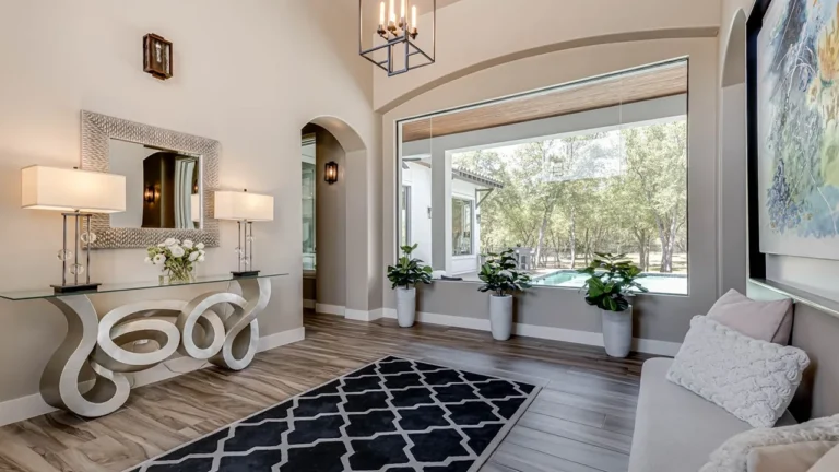 Entry sitting area with a sculptural scroll console, lantern pendant and a large window looking out to the pool