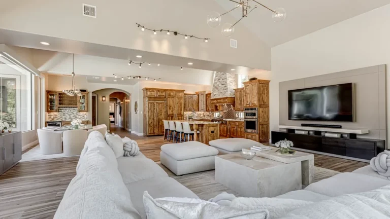 Great room with a white sectional and media wall open to the knotty alder kitchen, island seating and dining area under track lighting