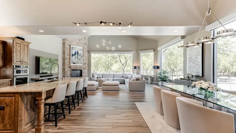 Long granite kitchen island with turned legs and counter seating beside a glass dining table, open to the living room's brick fireplace