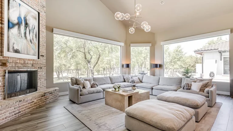 Living room with a brick fireplace wall, white sectional and ottomans beneath a glass-globe chandelier and vaulted ceiling