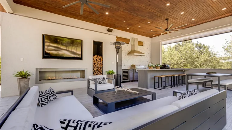 Covered outdoor living room with a sectional, linear fireplace and firewood niche, open to an outdoor kitchen and bar