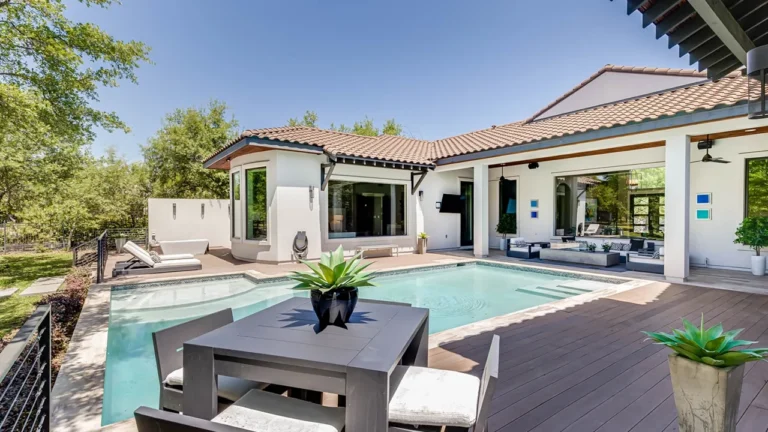 Backyard pool with a composite deck, poolside dining and agave planters behind a white stucco, clay tile roof home in The Dominion, San Antonio