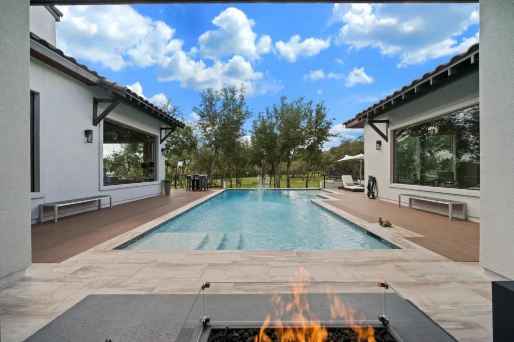 Backyard pool framed by covered patios with a fire table in the foreground at a Genesis custom home in The Dominion, San Antonio