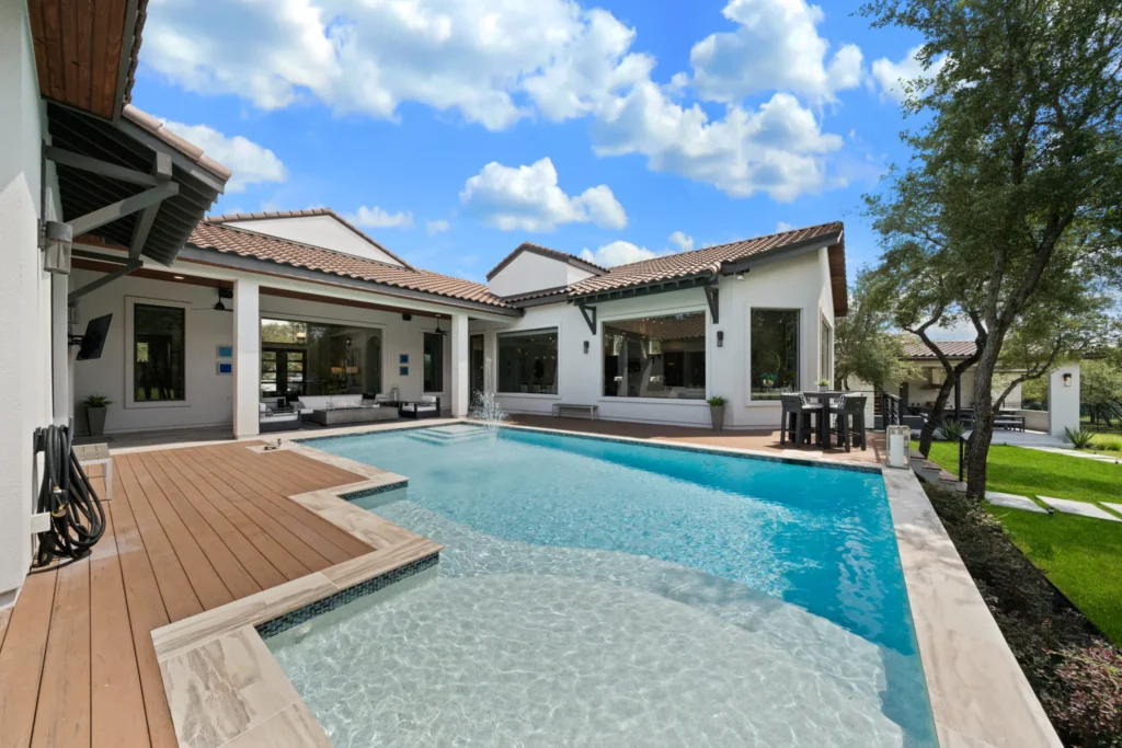 Rectangular pool with a tanning ledge and composite deck behind a white stucco, clay tile roof custom home in The Dominion, San Antonio