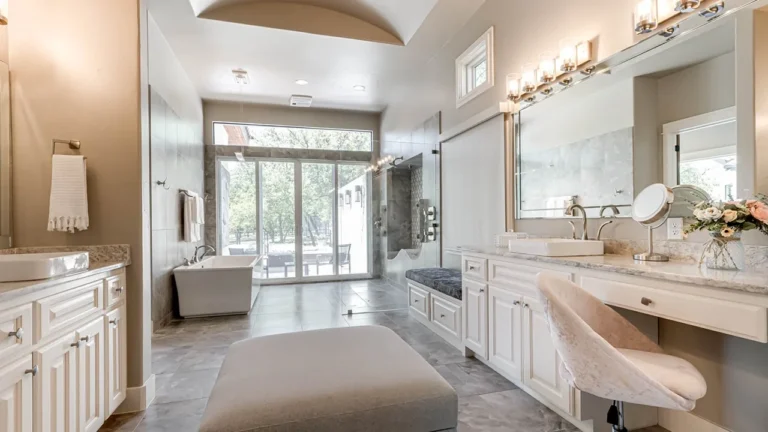 Primary bath with white double vanities, a seated makeup station and a freestanding tub in front of glass doors to the yard