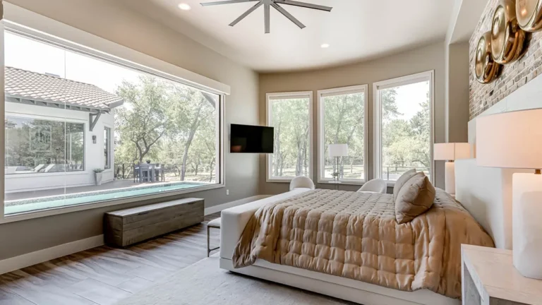 Primary bedroom with a wide picture window and bench overlooking the backyard, an oversized ceiling fan and wall-mounted TV