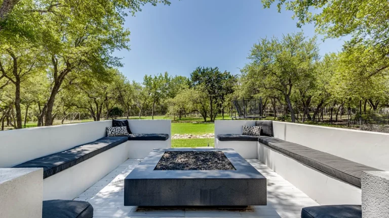 Sunken fire pit lounge with built-in cushioned benches and a square concrete fire table surrounded by live oaks