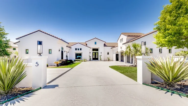 White stucco custom home with a clay tile roof, long entry drive, stucco entry pillars and agave plantings in The Dominion, San Antonio