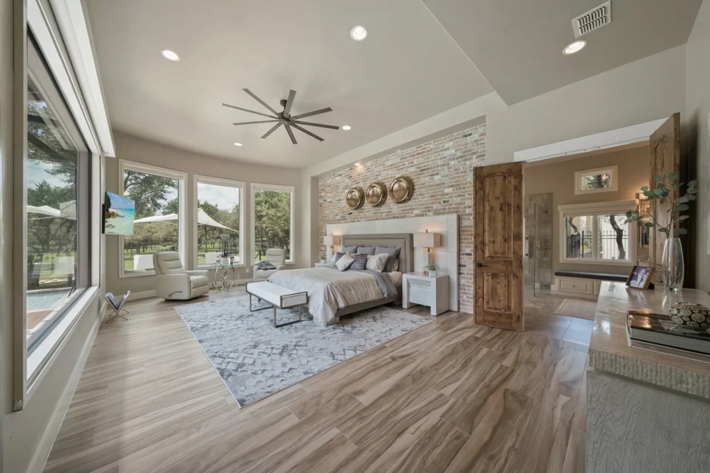 Primary bedroom with a brick accent wall, oversized ceiling fan and windows overlooking the yard in a custom home in The Dominion, San Antonio